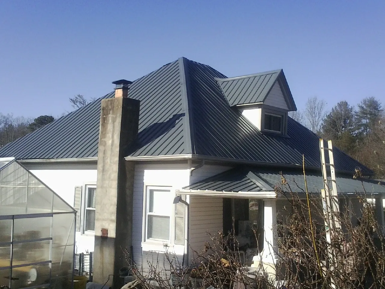 Dark blue standing seam metal roof on a white farmhouse with dormer — Slate & Tile Roof Repair by Roofing Brothers in Kingsville
