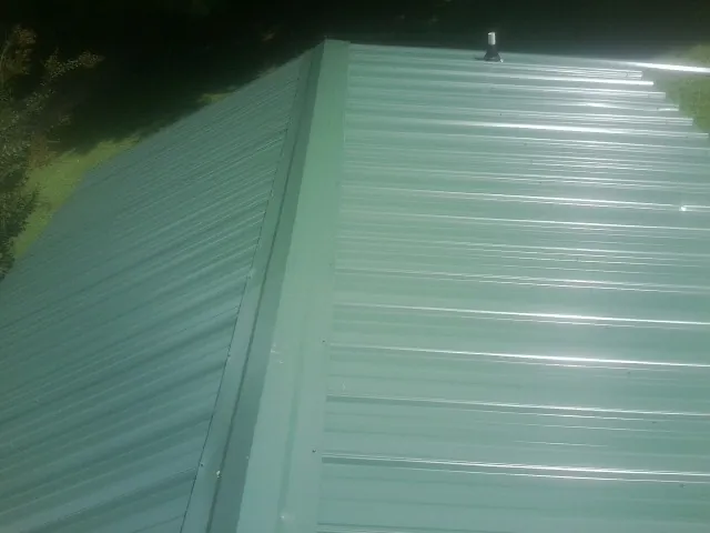 New green metal panels meeting at the ridge of a roof — Flat Roof Repair work by our crew in Kingsville