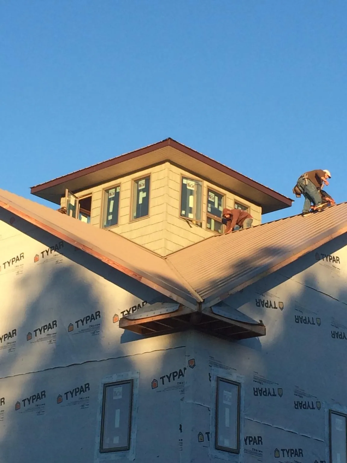 Roofers working around a rooftop cupola on a new metal roof at sunset in Kingsville